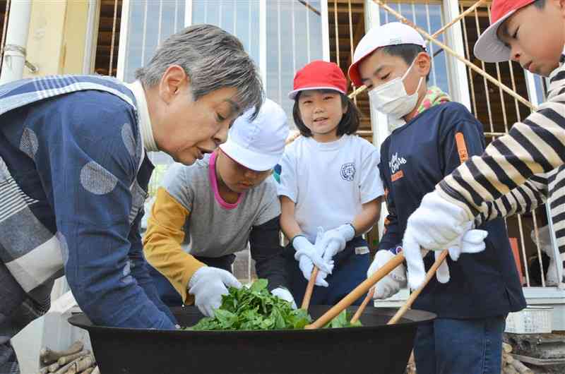 住民ボランティアの指導を受けながら、茶葉を釜でいる作業を体験する児童＝2日、天草市