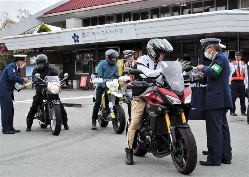 バイク愛好者に安全運転を啓発するチラシを配る熊本、大分両県警の警察官＝4月27日、南小国町