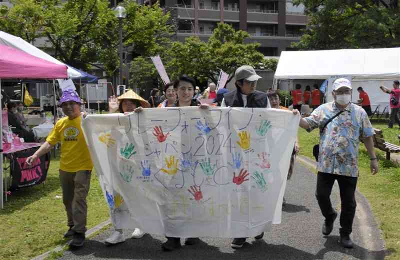 がん患者や家族への支援を呼びかけながら白川公園を歩く参加者＝11日、熊本市中央区