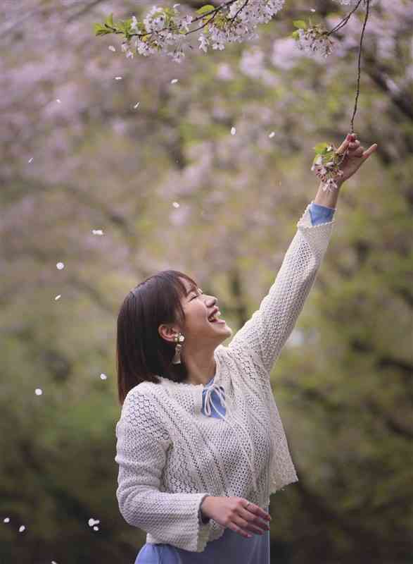 　【推薦】「桜色の笑顔」渡邉義弘（58）　熊本市＝熊本個人866　タイトル通り笑顔がすてきな写真です。望遠レンズと浅めの絞りで背景をぼかしたことで、主役のモデルと手にした桜が浮き上がり、すっきりした画面構成となりました。木々の緑や花びらなどは落ち着いた色調に仕上げられ、温かかな雰囲気が伝わります。