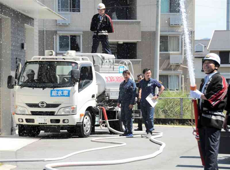 寄付されたタンク給水車にためた水を放水する消防団員ら＝17日、大津町