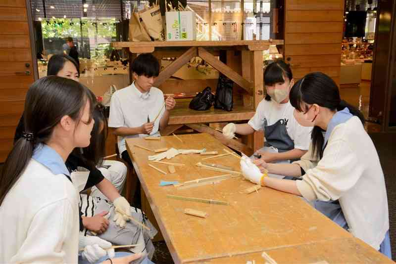 参加者に竹箸の作り方を教えるルーテル学院高の生徒ら＝18日、熊本市中央区