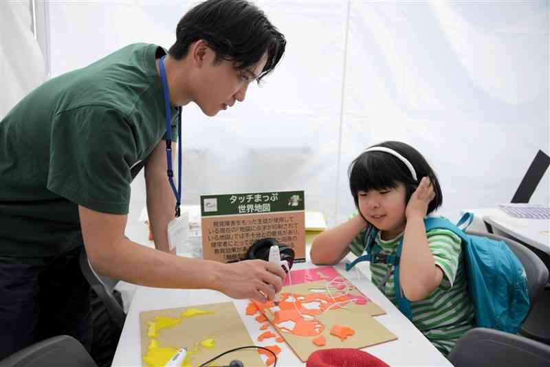 国の形のパーツを手で触り、音声で国名を学べる盲学校用の教材を体験する子ども（右）＝18日、熊本市西区