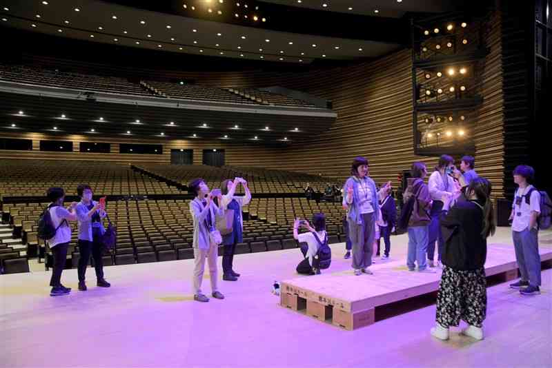 初めて開催された熊本城ホールのバックヤードツアーで、ステージに立って写真を撮る参加者たち＝18日、熊本市中央区