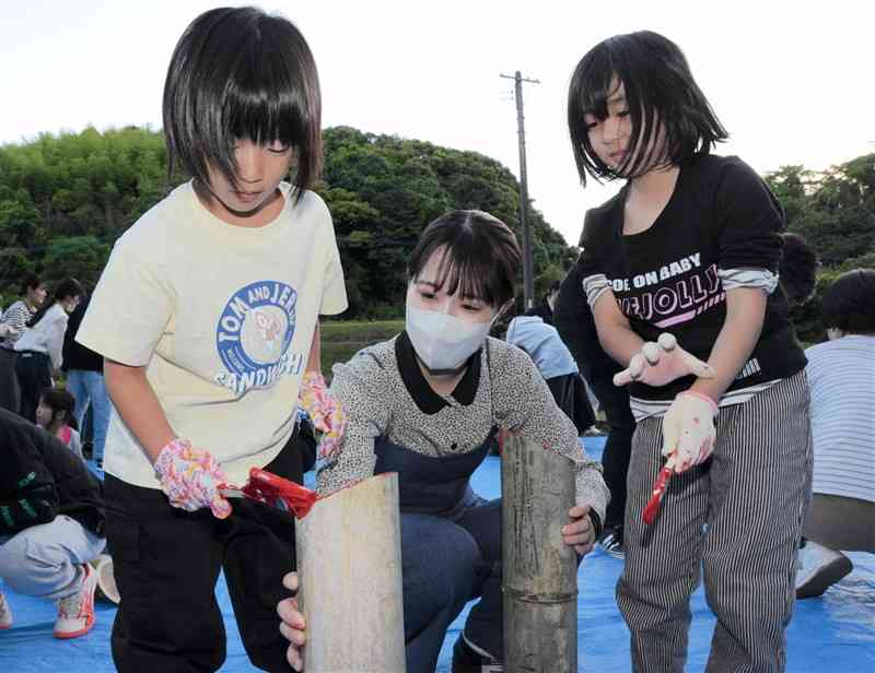熊本保健科学大の学生（中央）とともに、竹に色を塗る西里小の児童ら＝17日、熊本市北区
