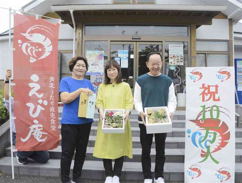 「芦北うたせ直売食堂　えび庵」の10万人目の客の岩井一隆さん（右）と真由美さん（中央）、遠山菊江代表＝24日、芦北町