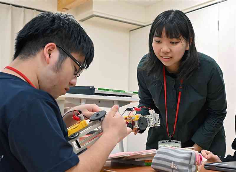 電気回路の仕組みについて学ぶ技術の授業で、2年の深瀬拓磨さん（左）にアドバイスする「学びのサポーター」の中島夏穗さん＝4月30日、熊本市中央区（上杉勇太）