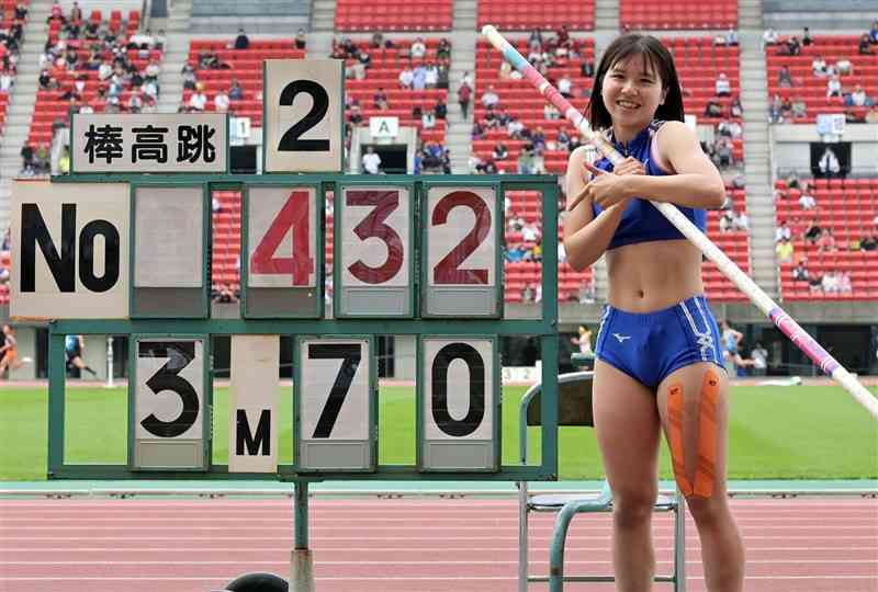 陸上女子棒高跳び決勝で、県記録を更新する3メートル70を成功し、ボードの前で笑顔を見せる志賀日向子（阿蘇中央）＝えがお健康スタジアム（谷川剛）