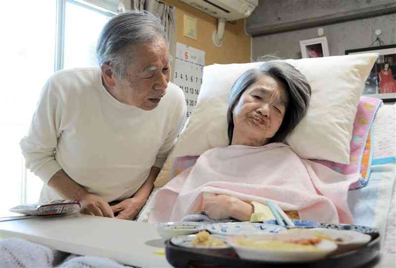 昼食を食べる水俣病患者の田中実子さん（右）と、優しく語りかける長姉の夫の下田良雄さん＝4日、水俣市