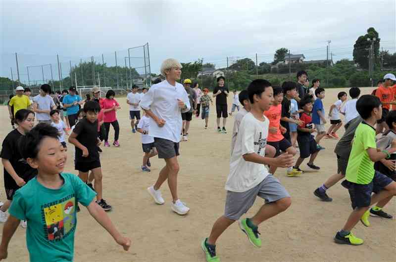 ランニング教室に参加した子どもたちに囲まれて走るタレントの三津家貴也さん（中央）＝8日、玉名市