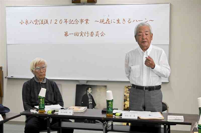 小泉八雲没後120年記念事業実行委員会の初会合であいさつする、ともに会長の副島隆氏（右）と西川盛雄氏＝13日、熊本市中央区