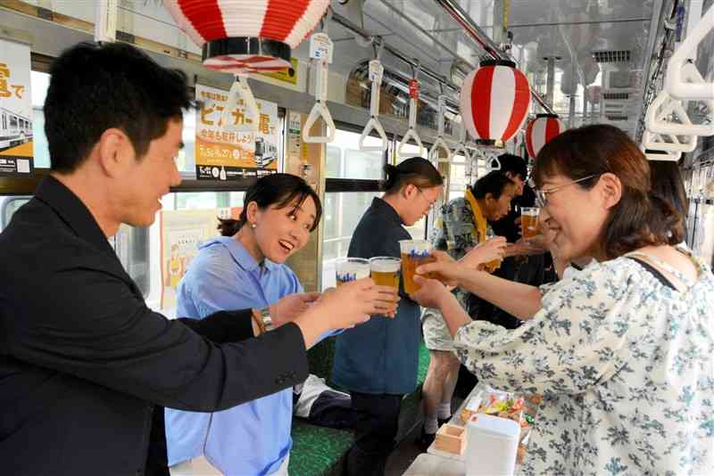 貸し切りの市電で乾杯する参加者たち＝21日、熊本市