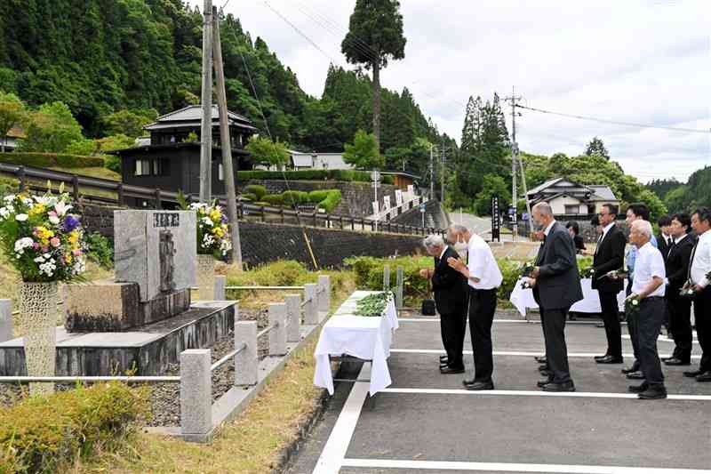 北里大水害の慰霊碑に献花する参列者。左奥は北里柴三郎記念館＝6月15日、小国町