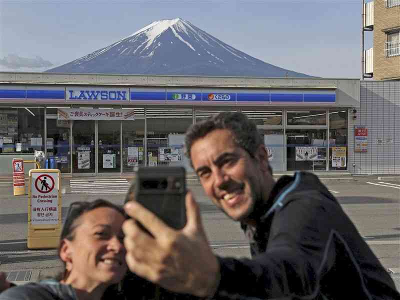 コンビニの屋根ごしの富士山を撮影する観光客ら＝5月、山梨県富士河口湖町（ロイター＝共同）