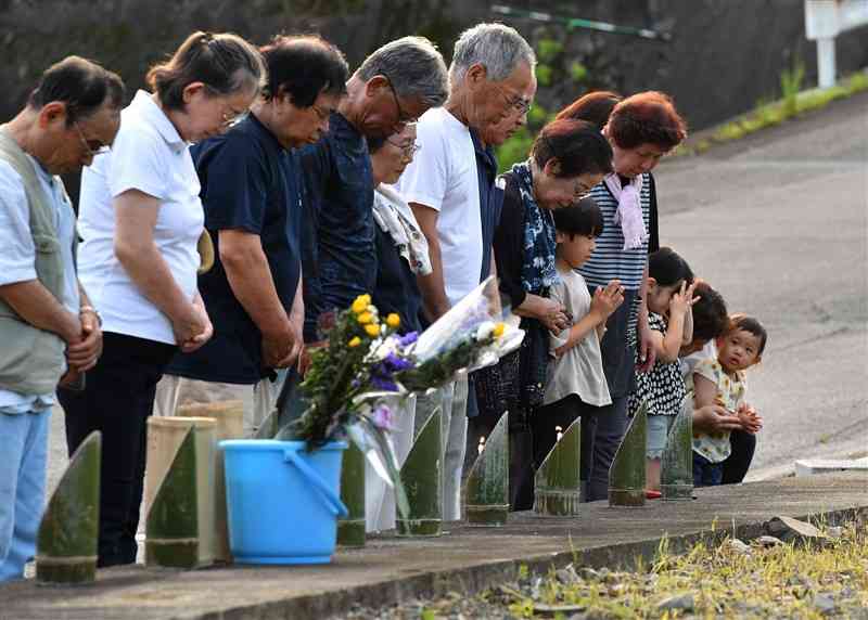 特別養護老人ホーム「千寿園」跡地で、亡くなった入所者の人数と同じ14基の竹灯籠に火をともし、黙とうする球磨村渡の小川集落の住民ら＝4日午後6時20分ごろ、球磨村（上杉勇太）