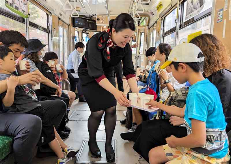 貸し切りの熊本市電で、日本航空の客室乗務員からジュースを受け取る子どもたち＝6日、熊本市中央区