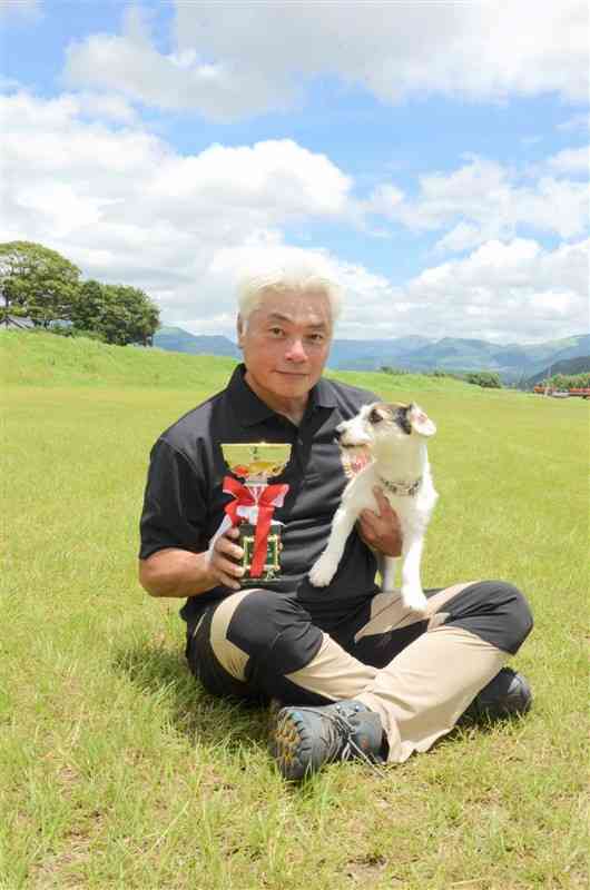 小型犬の全国大会で優勝し、トロフィーを持つ川口輝さんと愛犬トリクシー＝7日、大津町