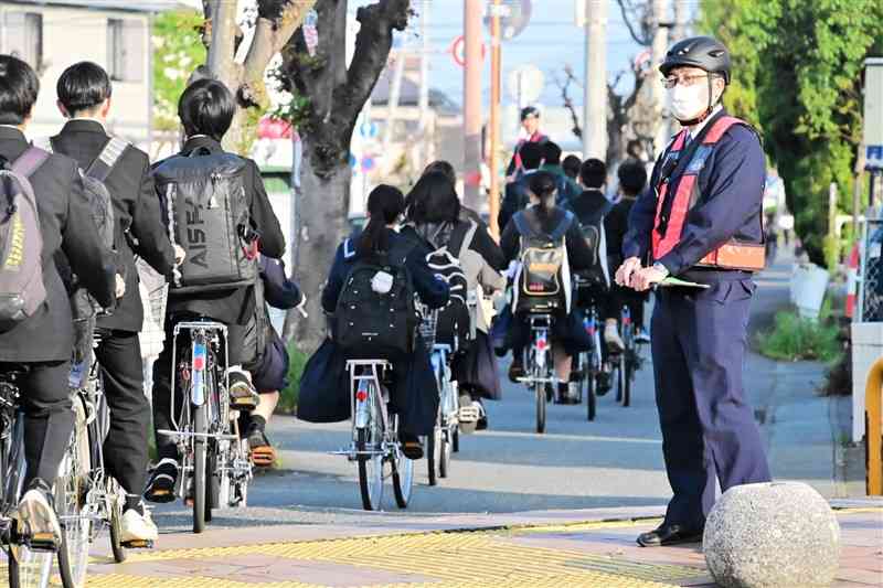 自転車で通学中の学生に交通指導する八代署員＝4月、八代市