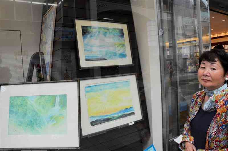 長崎書店で「山と川の物語」原画展を開いている池永久美子さん。ショーウインドーには、清流・川辺川の原画（上）も展示している＝16日、熊本市中央区