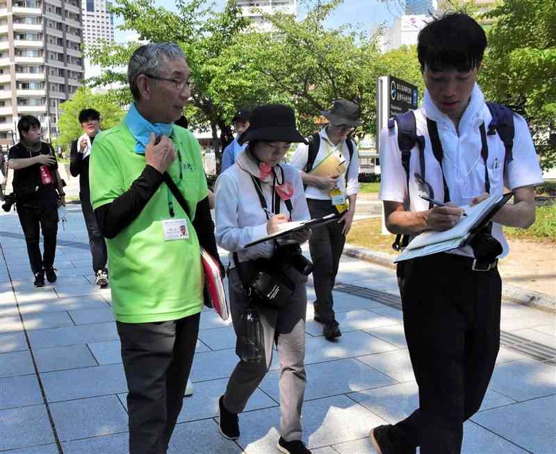 ピースボランティアの塚本誠さん（左）から話を聞く記者たち＝28日、広島市