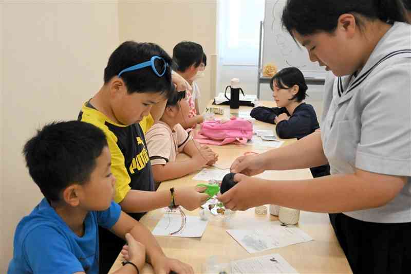 ペットボトルでのおもちゃ作りを子どもたちに教える菊池高生（右）＝7月28日、菊池市