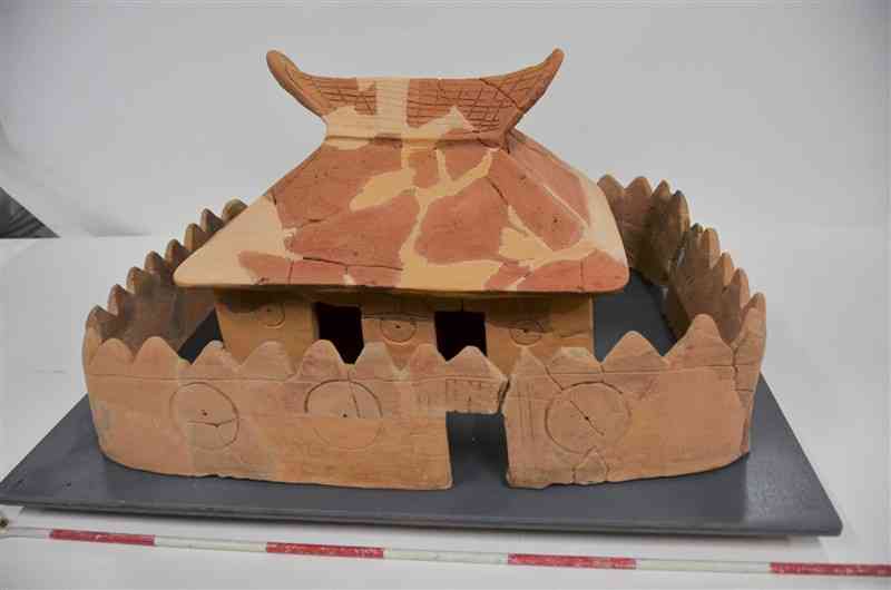 上官塚遺跡で出土した家形の埴輪と、囲い形の埴輪。色が赤い部分が出土したもので、薄い部分は復元（手前のポールの白色と赤色の部分は10センチ）＝嘉島町