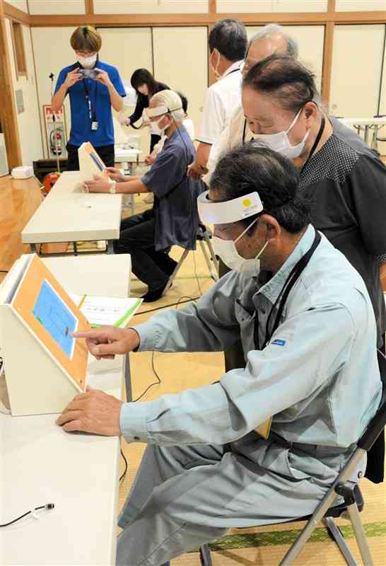 頭にセンサーを付けて脳活動チェックを体験する高齢者＝7月31日、阿蘇市