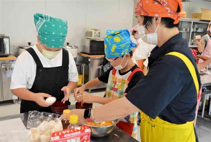 「わらびかみ」の木原成美理事長（右）から卵の割り方を学ぶ子どもたち＝1日、天草市