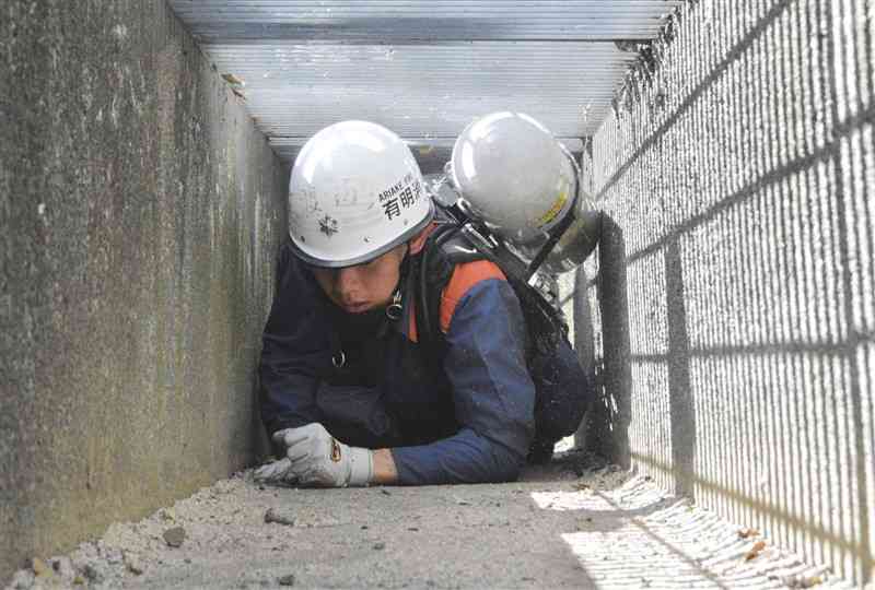 「狭所訓練」で空気ボンベを背負って側溝の中をはって進む熊本県消防学校の初任科生＝2日、益城町