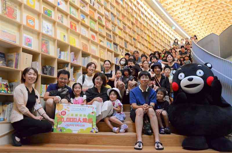 入館者2万人を達成し、記念撮影に納まる入館者ら＝12日、熊本市中央区