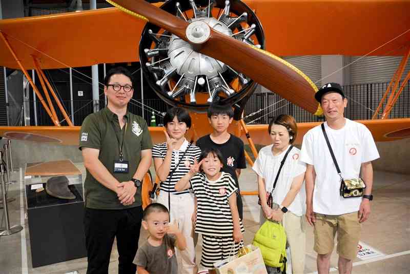 飛行機の展示の前で写真に納まる手柴智晴館長（左端）と松下貢史郎さん（右端）一家＝8月15日、錦町