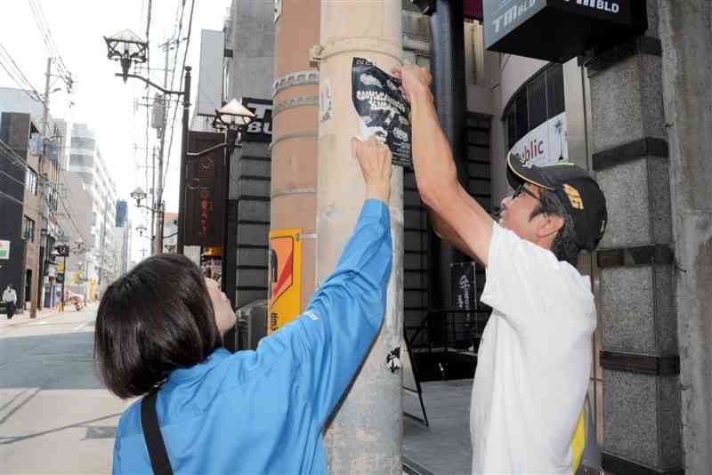 違反広告物を剝ぎ取る職員ら＝3日、熊本市中央区