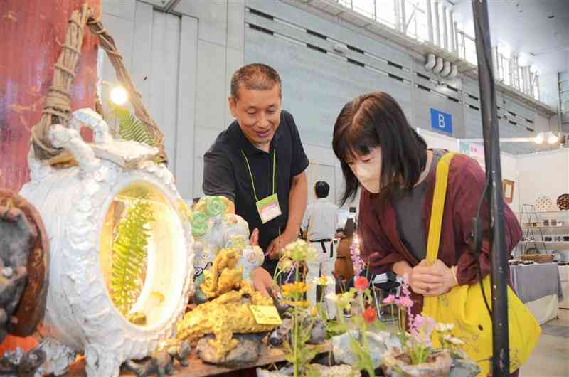 出店者（左）の話を聞きながら、陶器の置き物や花瓶を品定めする来場者＝5日、益城町