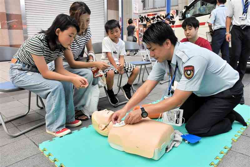 熊本市消防局の職員（右）からAEDの装着方法を学ぶ親子連れ＝7日、熊本市中央区