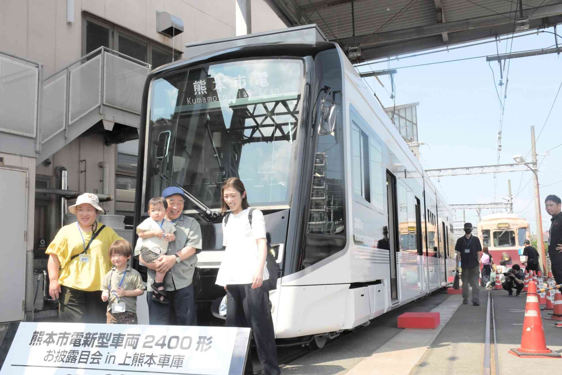 熊本市電の新型車両の前で記念撮影する参加者＝8日、同市西区