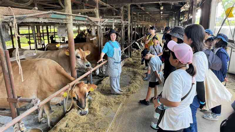 牛舎で、大薮真裕美さん（中央）の説明を聞く参加者たち＝7日、合志市