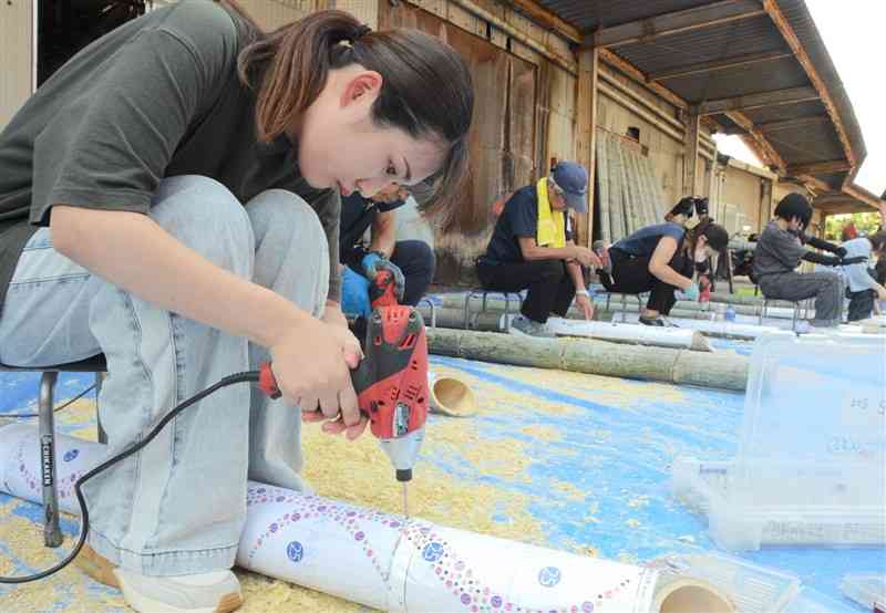 型紙を貼った竹にドライバーで穴を開けるボランティアの女性＝7日、熊本市北区