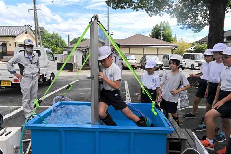 水圧がかかった状態のドアを開ける体験をする花房小の児童＝11日、菊池市