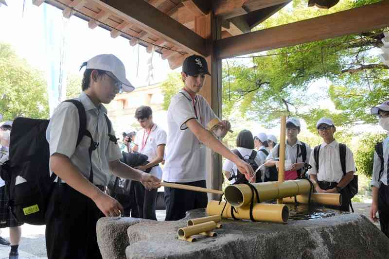 出水神社の手水舎で文徳中の生徒（左）と一緒に手を洗うペルーの生徒（中央）＝12日、熊本市