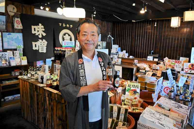 自社製品を手にする豊前屋本店5代目の吉良充展社長＝13日、高森町