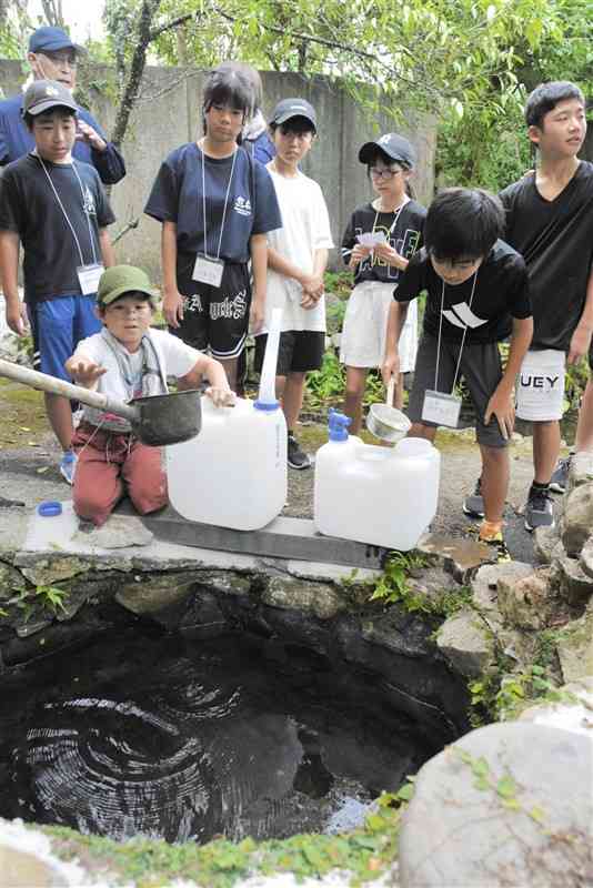 防災キャンプで、学校近くで湧き水をくむ水東小の児童ら＝14日、水俣市