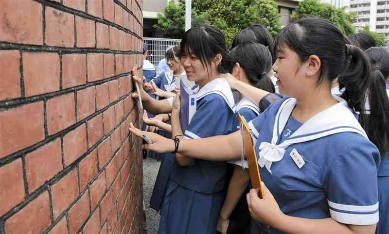 歩兵第13連隊の正門跡に手で触れる熊本学園大付属中の生徒＝21日、熊本市中央区