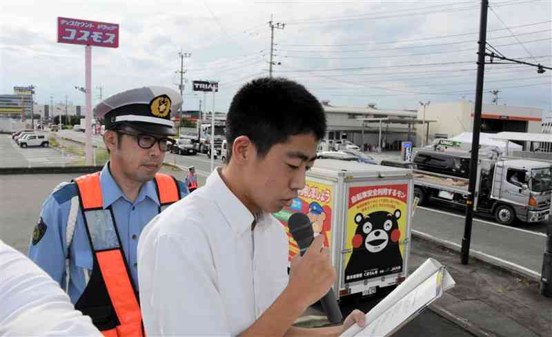 指揮車の上からマイクで交通安全を呼びかける翔陽高生。左奥はTSMC第1工場＝20日、大津町