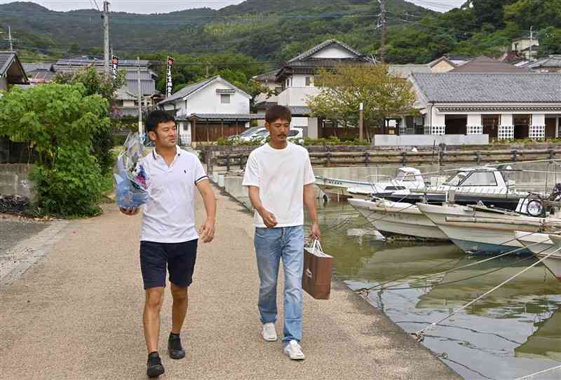 1999年9月24日の高潮災害で亡くなった小学6年生と、同級生だった野村和矢さん（左）と木村友規さん。花束を手に亡き友の自宅に向かった＝21日、宇城市不知火町の松合地区（小野宏明）