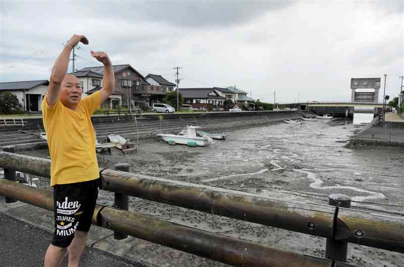 松合地区の集落中央にある船だまりで「高潮被害の時は高い波が次々と押し寄せた」と語る田中鉄也さん。右奥は被災後に設置された防潮水門＝8月21日、宇城市