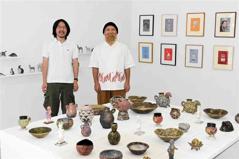 オープンした「UNDER　ROAD　GALLERY」で、企画展の作品に囲まれる佐藤かつあきさん（左）と松永健志さん＝23日、上天草市