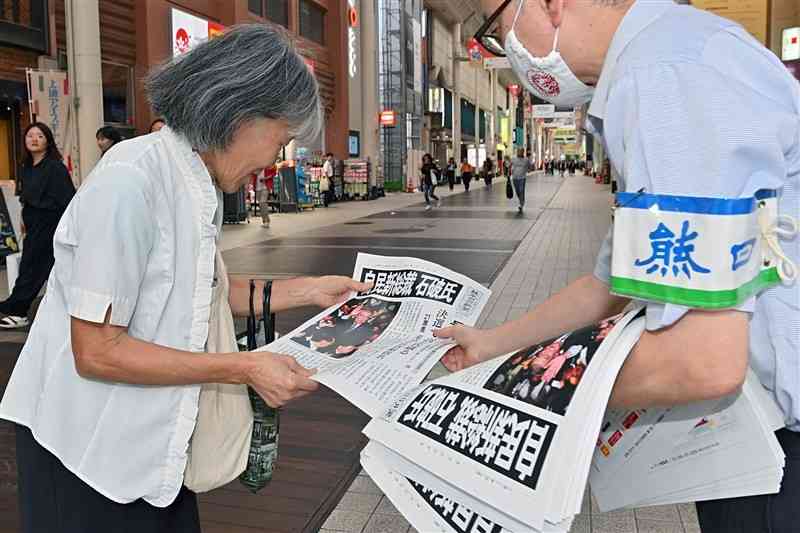 自民党総裁選で石破氏が選出された事を報じる熊日号外を受け取る通行人＝27日午後、熊本市中央区のびぷれす広場前（上杉勇太）