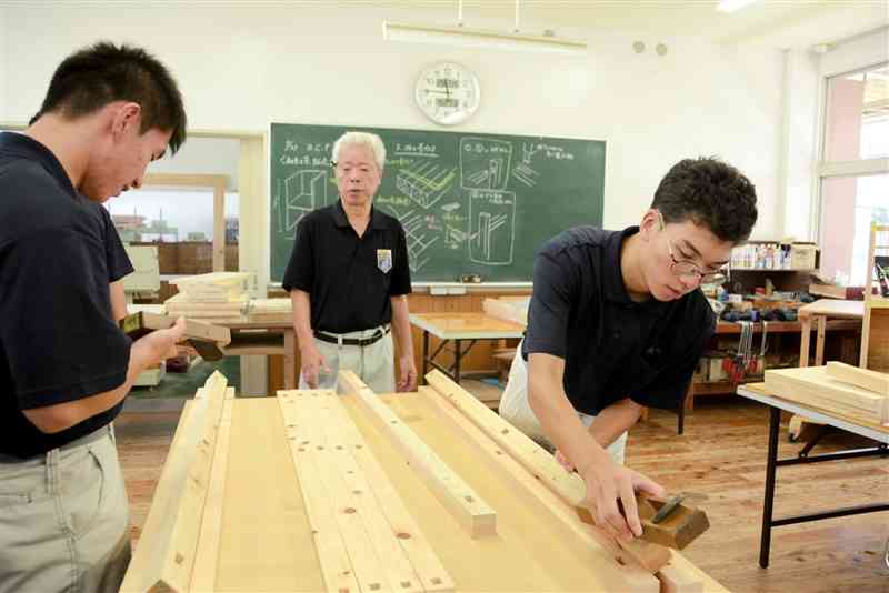 「ものづくりマイスター」の地元建具職人（中央）に技術を学びながら、陳列棚の製作を進める水俣高生＝27日、水俣市