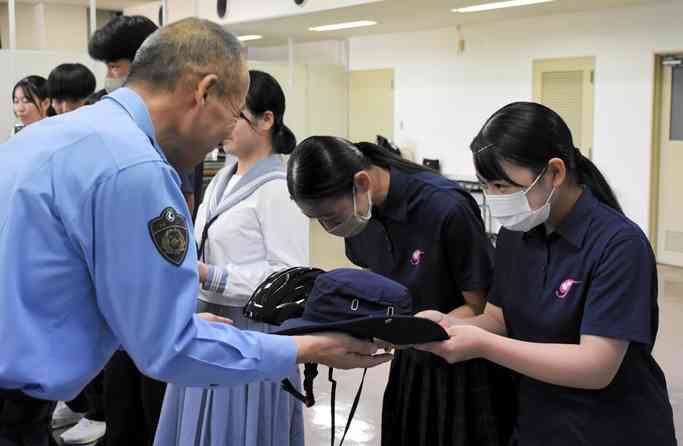 玉名署の髙橋太署長（左）からヘルメットを受け取る交通マナーアップ委員会の生徒＝9月13日、玉名市