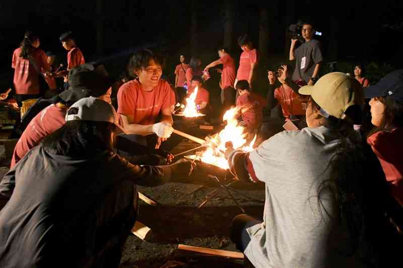 たき火でマシュマロを焼きながらスタッフと会話する子どもたち＝9月、阿蘇市